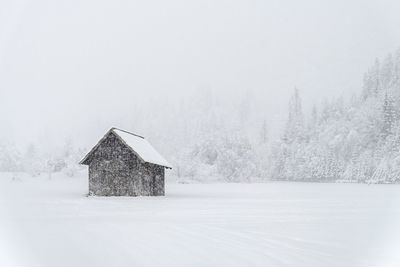 House on snow covered land and trees against sky