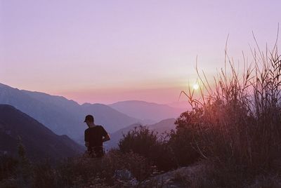 Rear view of silhouette man standing on mountain against sky during sunset