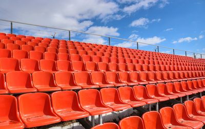 Empty red chairs at stadium against blue sky