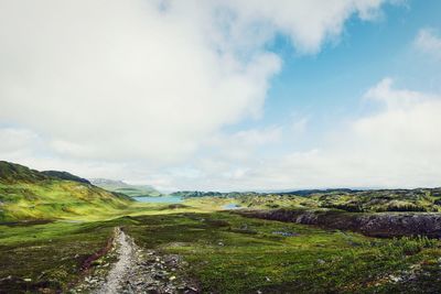 Scenic view of road amidst field against sky