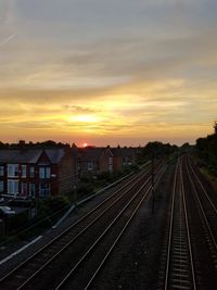 Railroad tracks in city against sky during sunset