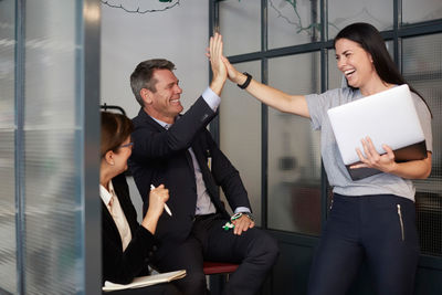 Cheerful creative businesswoman high-fiving with male bank manager during meeting in office