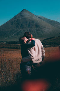 Woman sitting on field by mountain against sky