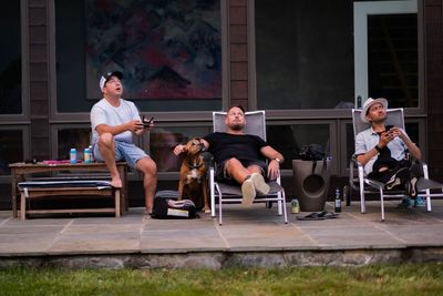 Man flying drone with friends and dog looking while sitting in yard