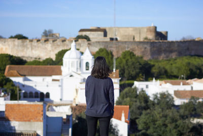Rear view of woman looking at buildings against sky