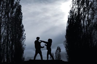 Silhouette man and woman standing by tree against sky