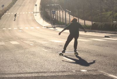 Rear view of people skateboarding on road