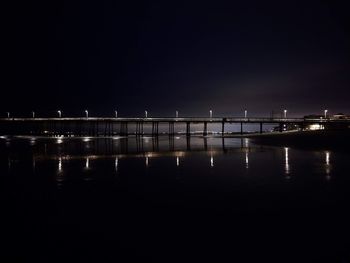 Illuminated pier over lake against clear sky at night