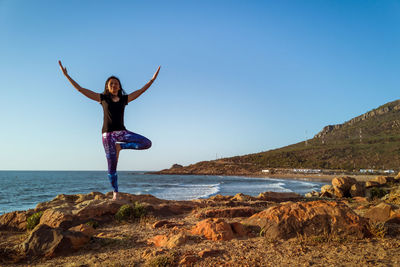 Woman standing on rock by sea against clear sky