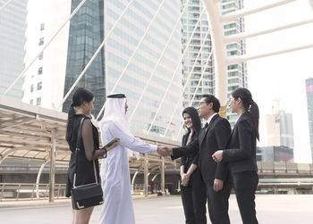 Male colleagues shaking hands while standing with businesswomen