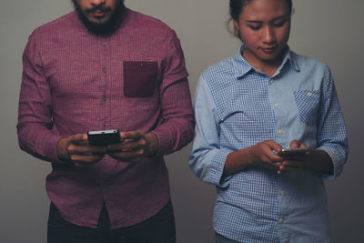 Midsection of man and woman using smart phone against gray background