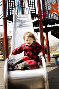 Portrait of cute girl sitting on slide at playground