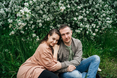 Young couple in love a girl and a man sit on the grass of a flowering apple tree 