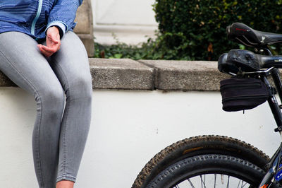 Midsection of woman sitting on retaining wall by bicycles