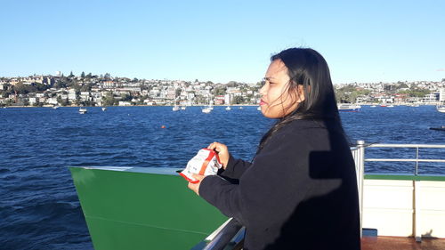 Woman standing by sea against sky in city