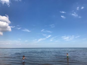 Siblings playing in sea against sky