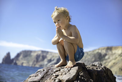 Low angle view of shirtless man sitting on rock against clear sky