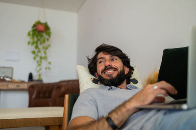  man working at home from his couch with laptop on his lap. man lying down.  notebook for working.