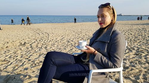 Woman having coffee while sitting at beach