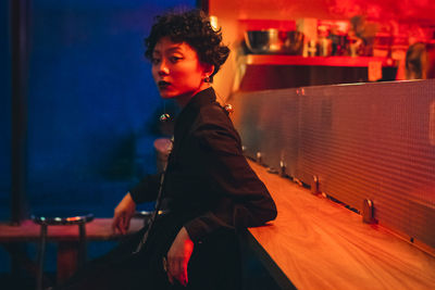Portrait of woman looking away while sitting in illuminated nightclub