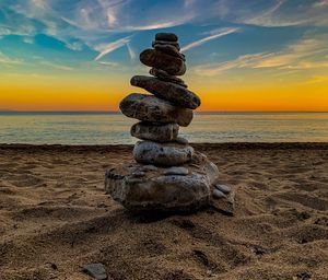 Stack of pebbles on beach against sky during sunset