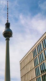 Low angle view of berliner fernsehturm against building with windows and cloudy sky 