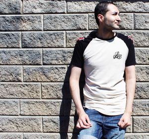 Young man looking away while standing against stone wall