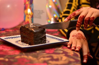 Cropped image of woman cutting birthday cake at table