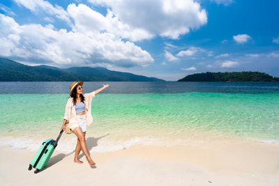 Rear view of woman standing at beach against sky