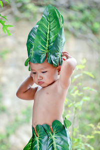 Cute boy wearing leaves and garland standing outdoors