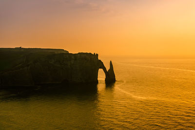 Silhouette rock formation by sea against sky during sunset