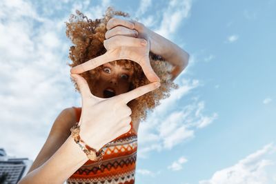 Low angle view of woman with arms crossed against sky