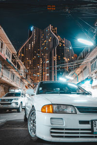 Cars on illuminated street by buildings in city at night