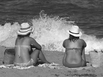 Rear view of friends in bikini sitting on sandy beach