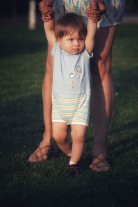 Cute mother and baby boy with blonde hair on grass making first steps