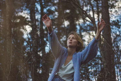 Young woman with short hair dancing against trees in forest