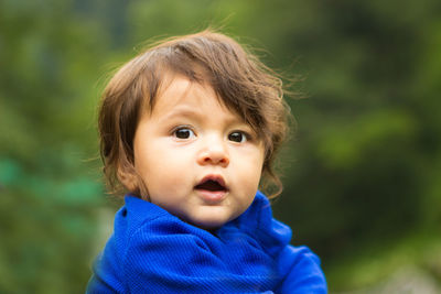 Close-up of cute baby boy looking away against trees