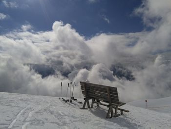 Scenic view of snow covered bench against sky