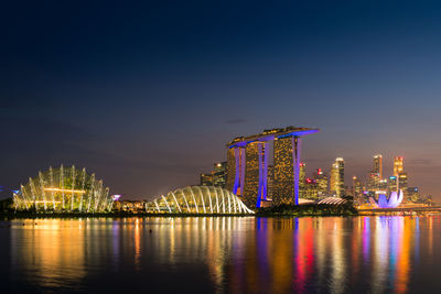 Illuminated city by river against sky at night