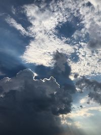 Low angle view of sunlight streaming through clouds