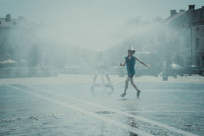 Playful girl enjoying water spraying from fountain at town square