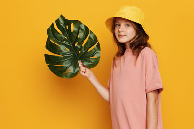 Portrait of young woman standing against yellow background