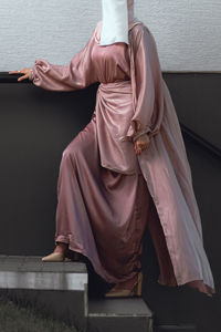 Full length image of veiled woman with white niqab and pink silky dress standing on the stairs