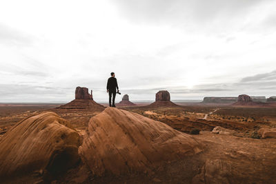 Rear view of man standing on rock against sky