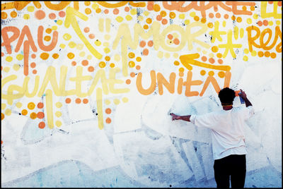 Rear view of man standing against graffiti wall