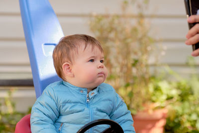 Boy toddler in his push car interacting with family via video conference on the cell phone