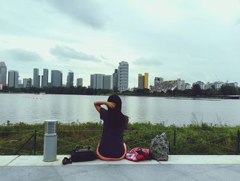 Rear view of woman sitting on walkway against river in city