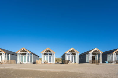 Beach huts in row against clear blue sky