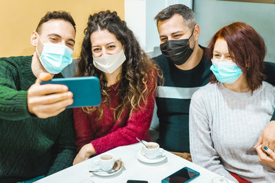 Cheerful friends wearing mask while doing selfie at cafe