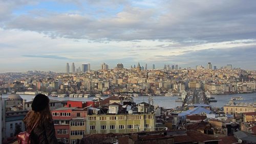 Rear view of woman looking at cityscape against cloudy sky